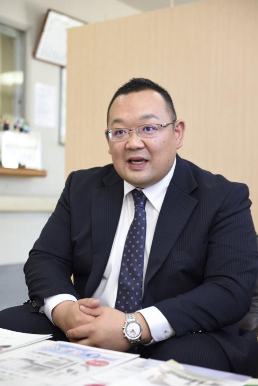 インタビュー画像:木目調間仕切り版の前で椅子に座り、これから介護者を目指す方へコメントされている荒巻さんの様子
