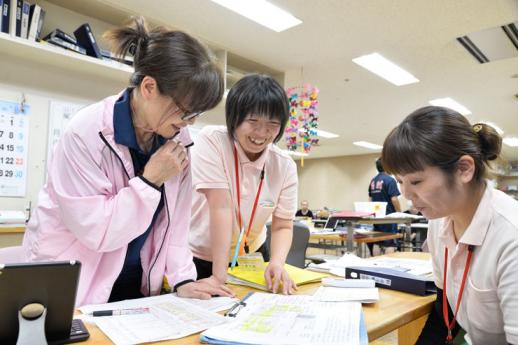 画像:施設内のスタッフルームの机を3名の女性介護スタッフが囲み机の資料を見ながら会話している様子