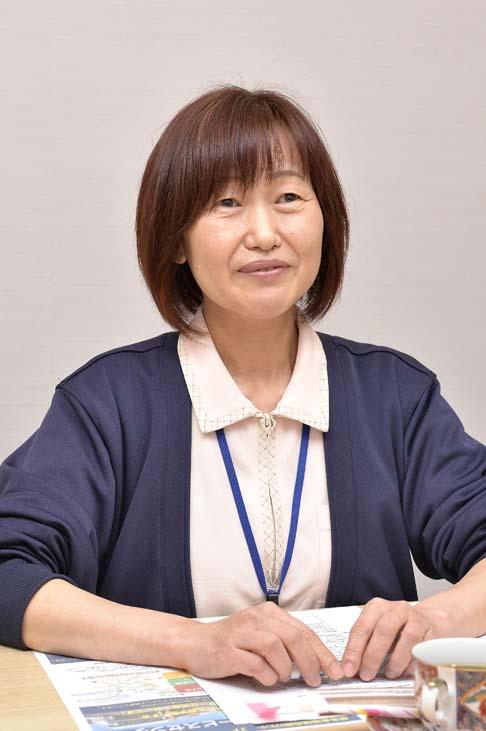プロフィール写真:白い壁の部屋で、両手を机の上に置きインタビューに答える岩永さんの様子。