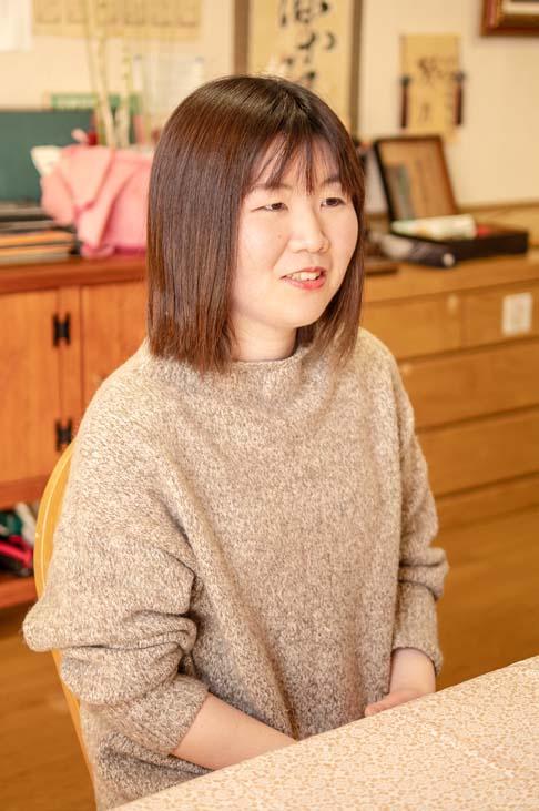 プロフィール写真:施設内の事務室で椅子に座り両手をテーブルの下においてインタビューに答える渡邉さんの様子