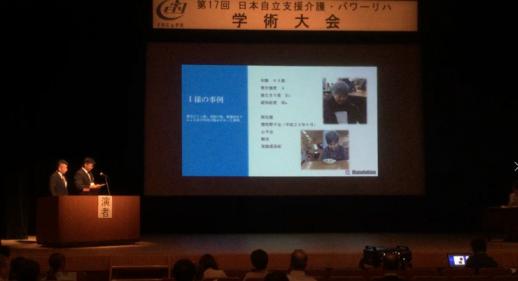 画像：日本自立支援会議の学術大会で壇上で２名の方がスライドを投影しプレゼンしている様子
