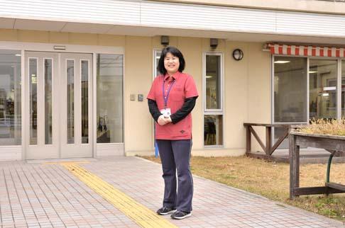 画像:肌色の壁にタイル張りの通路で軽く前で手を組みカメラに映る原田さんの様子。