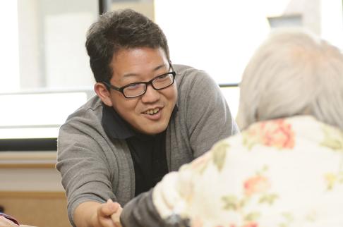 画像:女性の利用者の方の右手を軽く支えながら目線を合わせている川畑さんの様子。