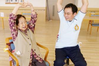 画像：屋内で体操されている女性の利用者と一緒に体操指導されてる志田さんの様子