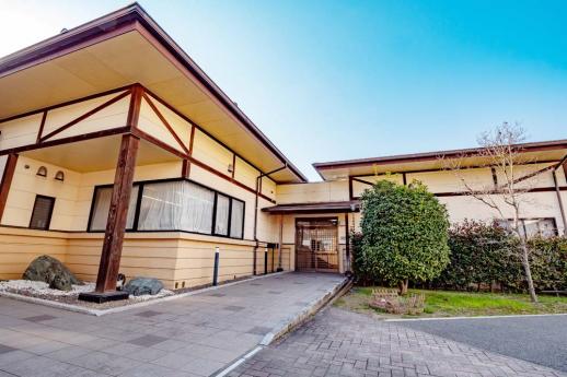 画像:青空を背景に中央にアプローチがあり右側の庭のあるL字型の施設の全景の様子