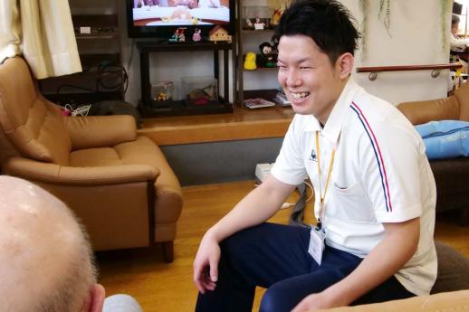 画像:施設内でソファーに座っている男性利用者と椅子に座って利用者を見ながら談笑する脇田さんの様子