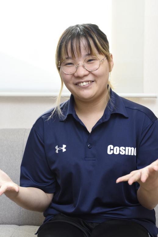 プロフィール写真:白い壁の部屋でソファに腰かけ、両手を広げて笑顔でインタビューに答える松門さんの様子