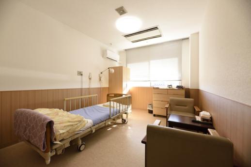 画像：介護用ベットにロッカーと引き出しと小さな応接が配置された施設内の明るい居室の様子