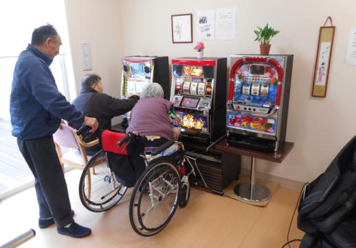 画像:施設内でスロットゲーム3台のうち2台の前に利用者が遊んでおり1名の利用者が後ろから眺めている様子