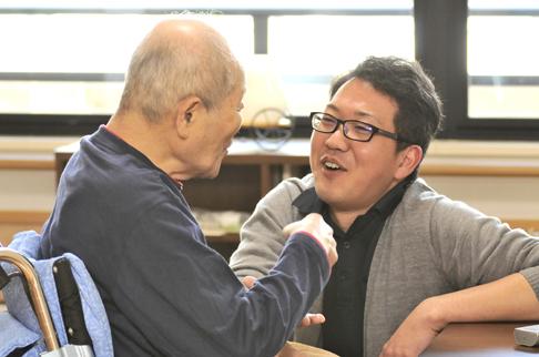 画像:車椅子に座っている利用者の方と目線を合わせ話している川畑さんの様子。