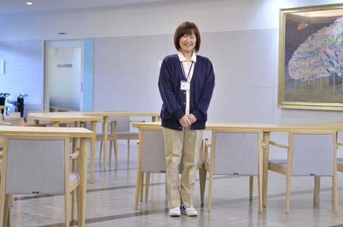 画像:共有スペースの机の前で立った状態で手を前で組みカメラに映る岩永さんの様子。