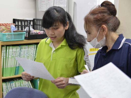 画像：施設内で一人の女性研修生が紙を両手に持ち、そのそばで指導している女性職員の様子