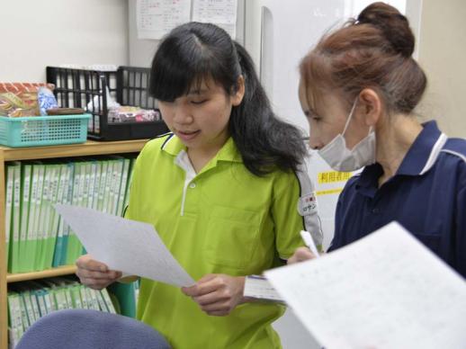 画像:施設内で一人の女性研修生が紙を両手に持ち、そのそばで指導している女性職員の様子