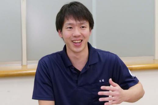 画像:すりガラスの窓のある施設の中で、左手を前にして話をしている江頭さんの様子