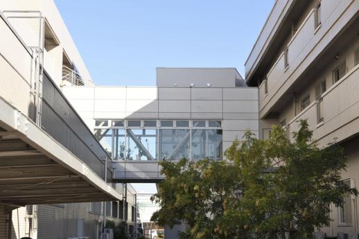 画像：青空を背景に大きな３階建ての建物の間の中２階に渡り廊下のある施設の様子