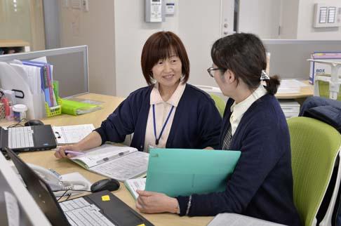 画像:パソコンの前で黄緑の椅子に座って女性スタッフと話している岩永さんの様子。