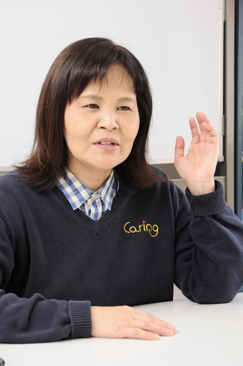 プロフィール写真:ホワイトボードの前で座った状態で机の上に右手を置き左手は軽く上げている中島さんの様子。