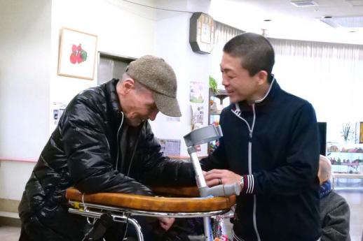 画像:施設内で手押し歩行器を使って前に歩こうとしている利用者の介護をしている脇田さんの様子