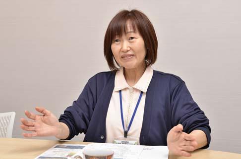 画像:白い壁の部屋で、左手は机の上に置き右手は机から少し上げてインタビューに答える岩永さんの様子。